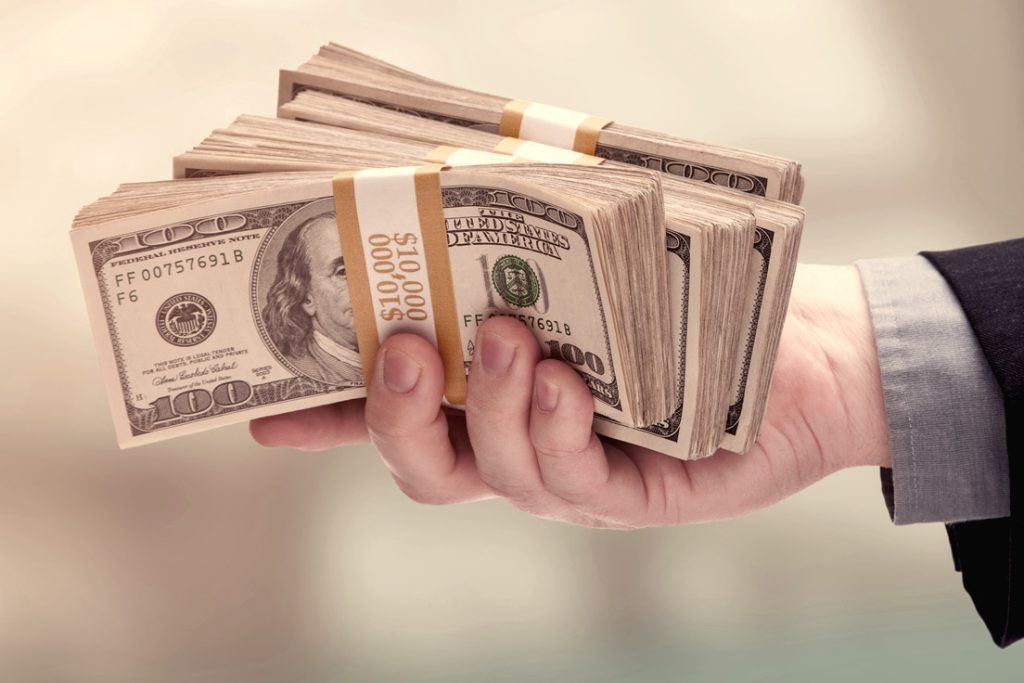 A hand holding bundles of $100 dollar bills.
